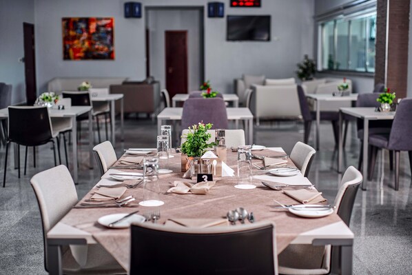 Un comedor moderno con mesas dispuestas para cuatro, cada una con un número, copas, cubiertos y un centro de mesa.