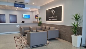 A hotel reception area with a reception desk, a sofa, and a wall-mounted sign. - Sami Court Airport Hotel Abuja (Abuja)