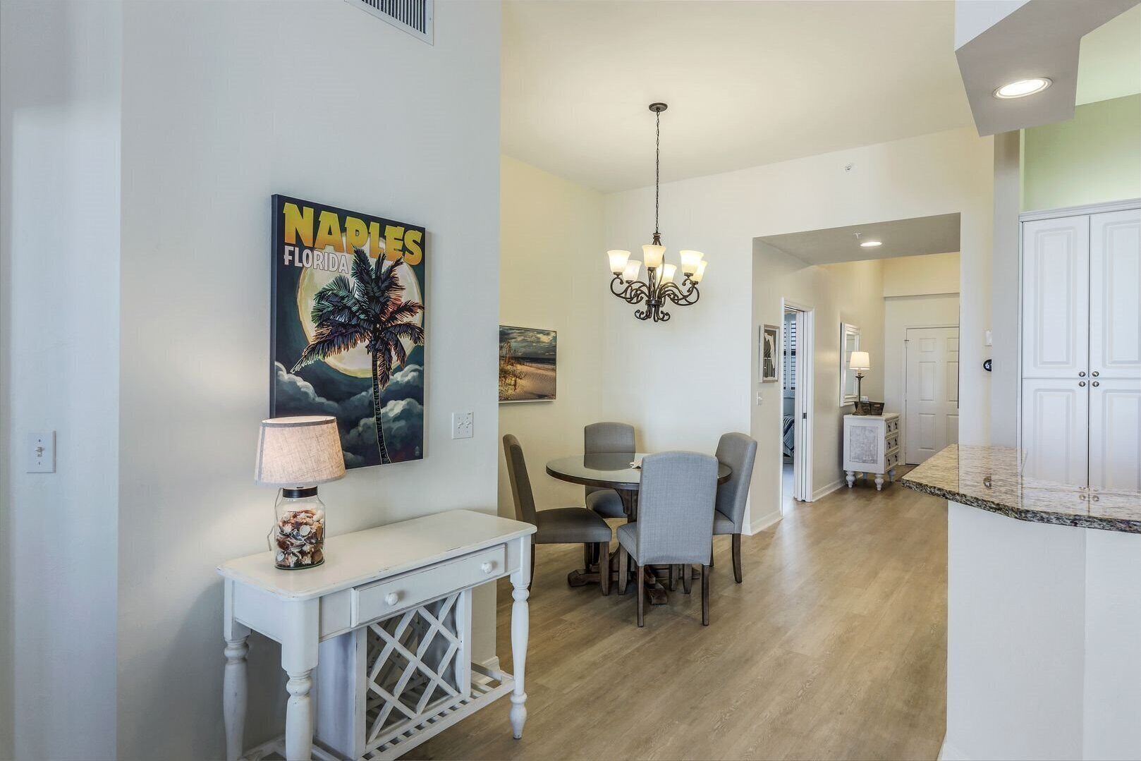 A dining area with a table and chairs, a chandelier, and a wall-mounted painting of a palm tree and moon.