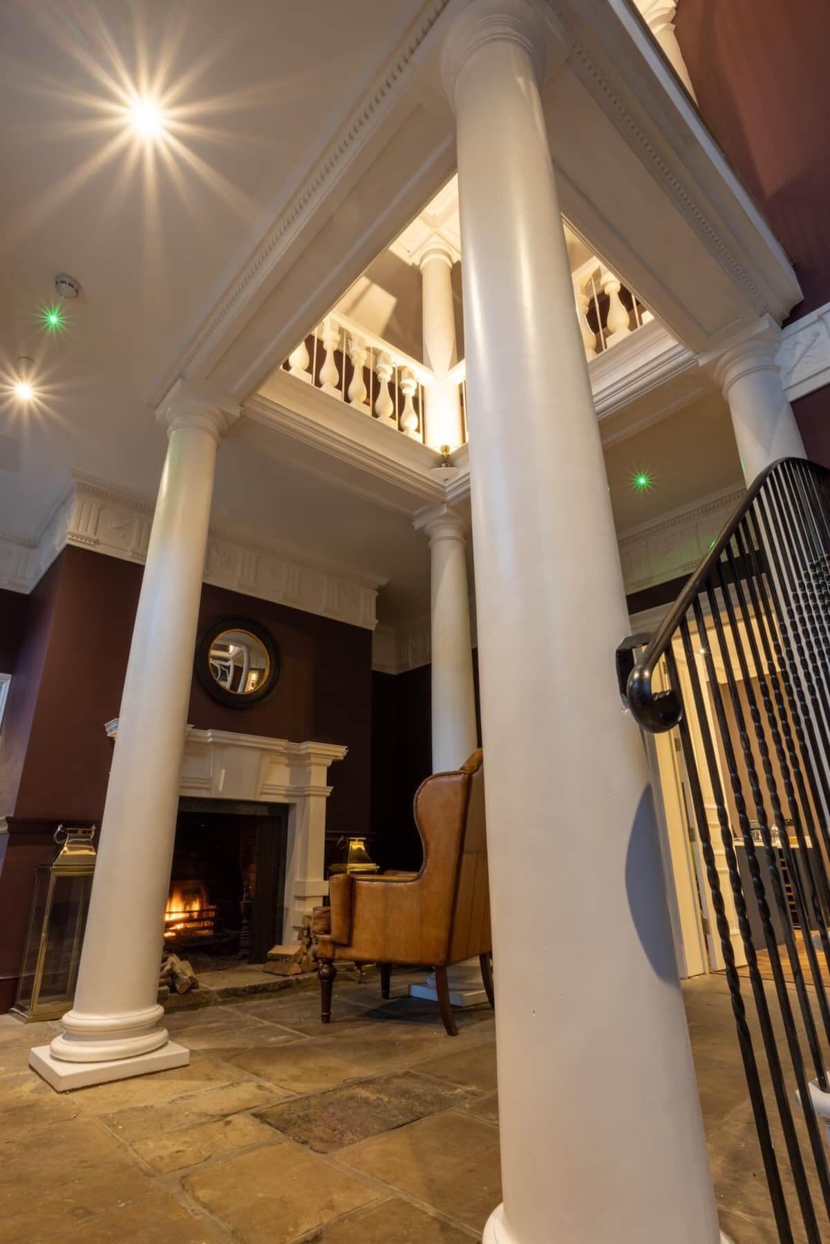Un vaste hall d’entrée avec des colonnes blanches, une cheminée et un escalier.