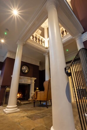 A grand foyer with white columns, a fireplace, and a staircase.