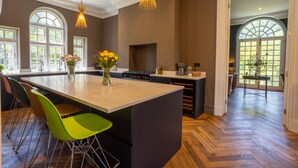 Une cuisine spacieuse dotée d’un grand îlot central, de luminaires suspendus modernes et d’une vue sur un jardin, accessible par une porte vitrée.