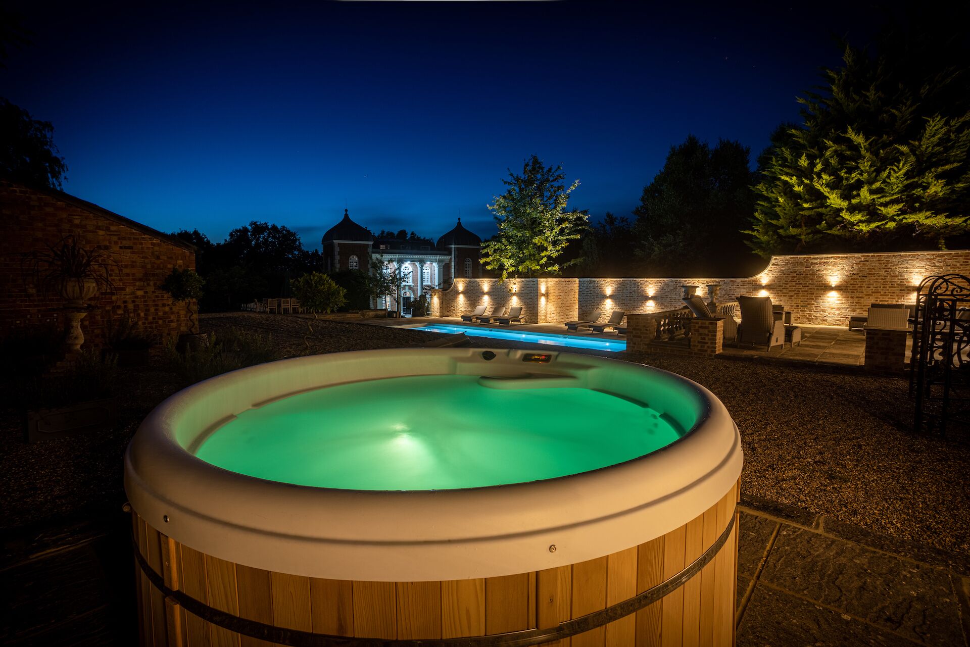 Un jacuzzi installé dans un jardin, avec un mur en briques et un espace salon extérieur.