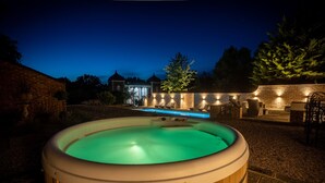 Un jacuzzi installé dans un jardin, avec un mur en briques et un espace salon extérieur.