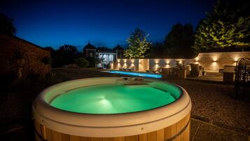 Un jacuzzi installé dans un jardin, avec un mur en briques et un espace salon extérieur.