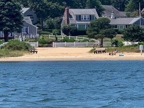 A beach with a sandy shore, a wooden bench, and a white picket fence.