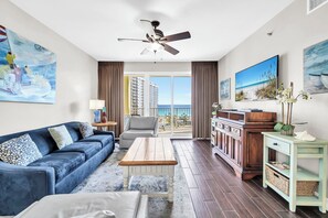 A living room with a blue sofa, a wooden coffee table, a TV, and a view of the ocean.
