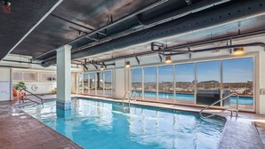 Ein Hallenbad mit großen Fenstern, Blick auf die Stadt und einer Decke mit freiliegenden Rohren.