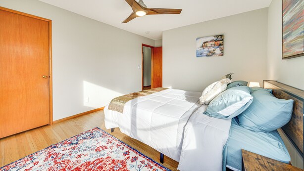 A bedroom with a bed, a ceiling fan, a wooden door, a painting, and a rug. - Quaint Renton Home ~ 15 Mi to Downtown Seattle! (Renton)