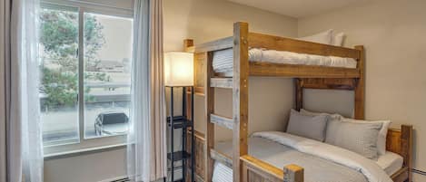 A bunk bed with a wooden frame, a bedside lamp, and a view of the outside through a window with curtains.