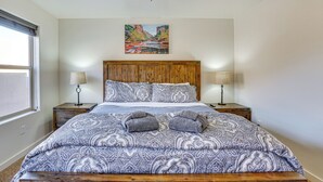 Ein Schlafzimmer mit einem Holz-Kopfteil, einem großen Bett mit gemusterten Betttextilien, zwei Nachttischlampen und einem Wandbild einer Schlucht.