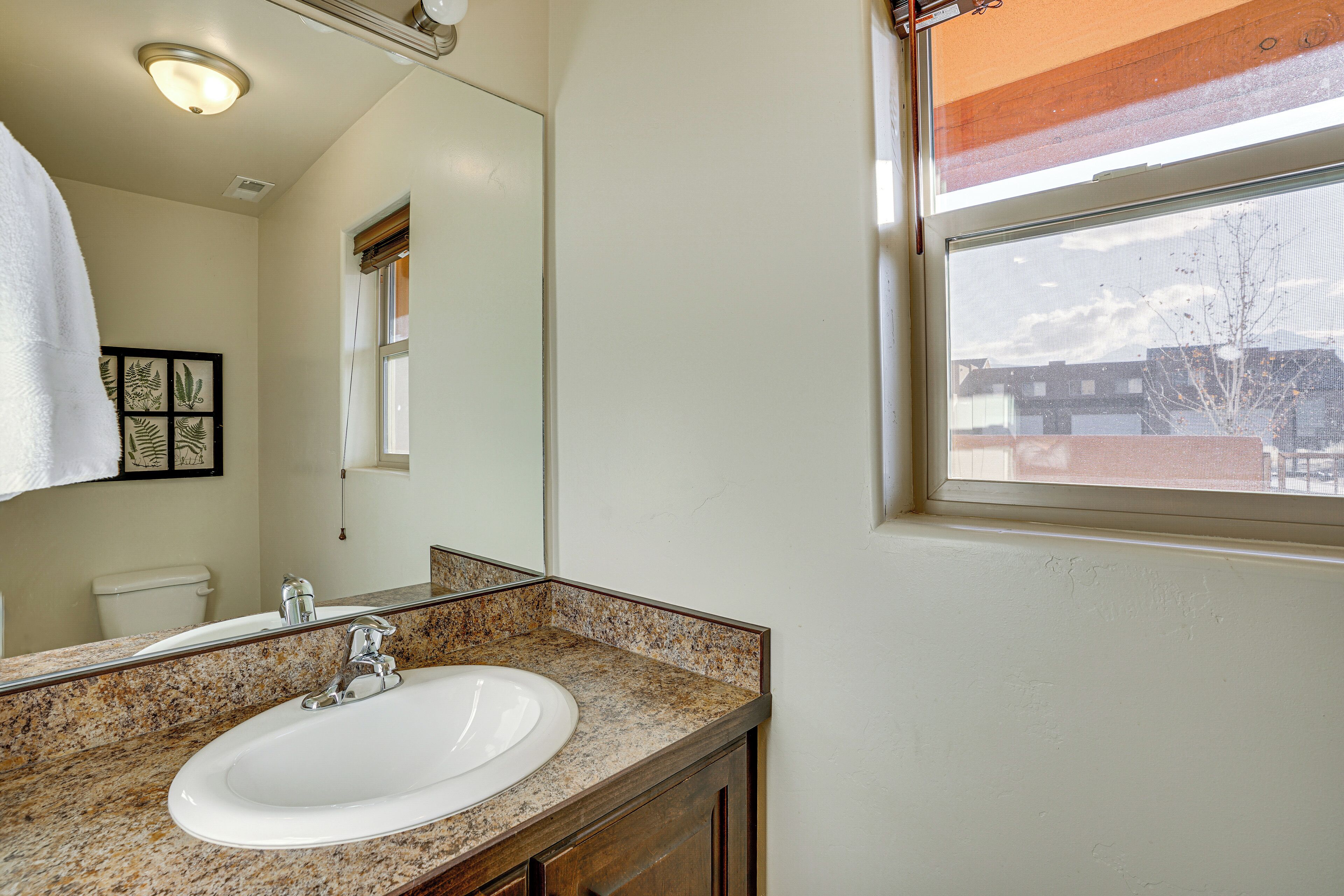 A bathroom with a granite countertop sink, a mirror, and a window with a view of buildings and trees.