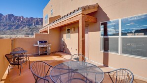 Eine Terrasse mit rundem Tisch und Stühlen, einem Grill und Blick auf die Berge.