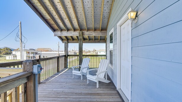 A wooden deck with two white Adirondack chairs, a covered area with a wooden ceiling, and a light fixture on the wall. - Walk to Crystal Beach! Family & Pet-friendly Haven (Port Bolivar)