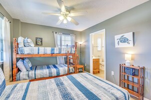 A bunk bed room with a ceiling fan, a bedside table, and a wall-mounted shelf with books.