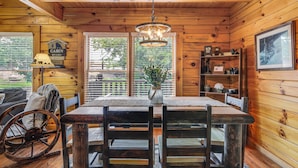 L’intérieur d’une cabane avec une table à manger en bois, des chaises, un lustre et une vue à travers la porte.