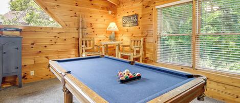 A pool table with balls, a billiards sign, and a lamp in a wooden room with a window.