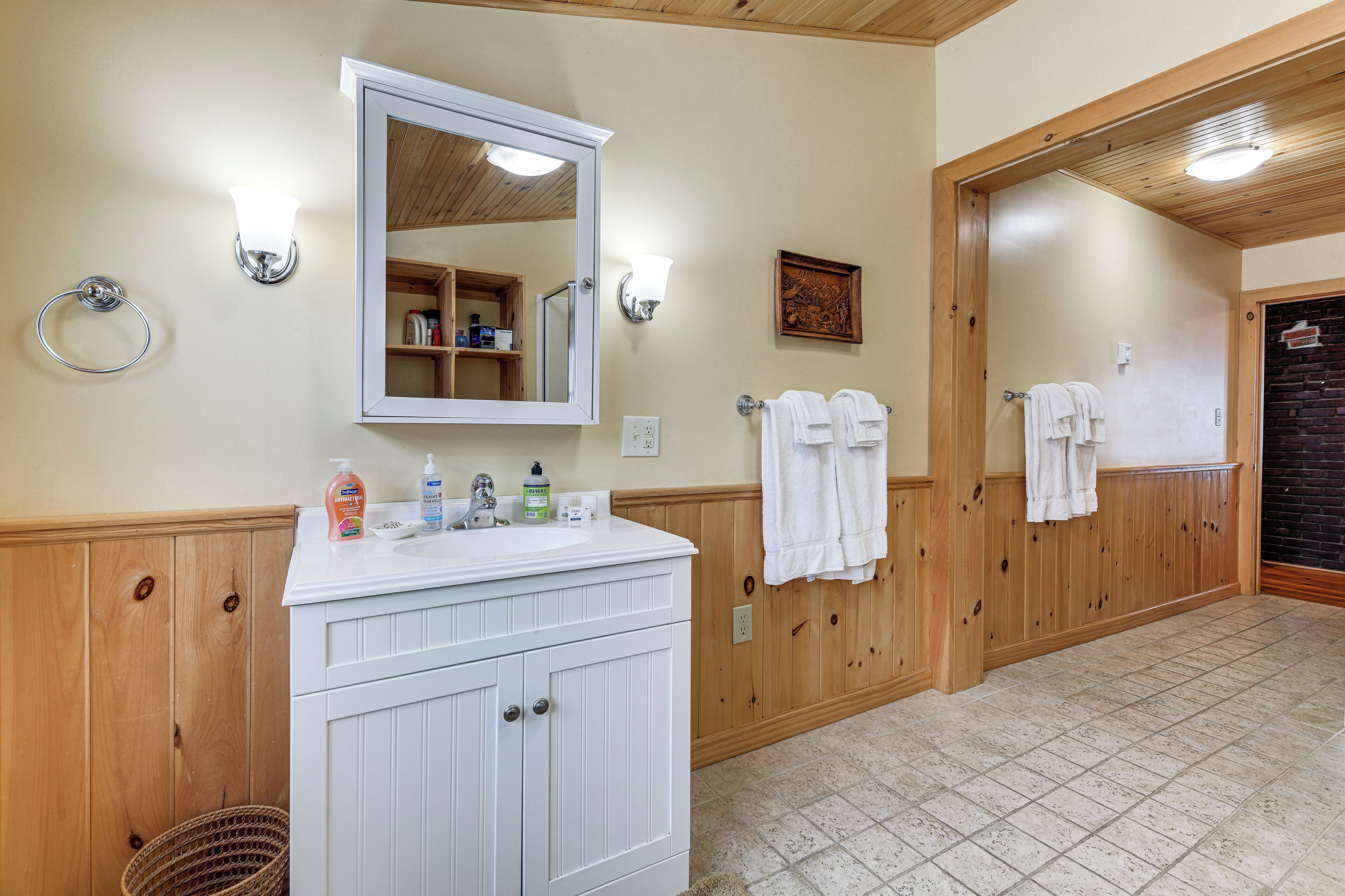 A bathroom with wooden paneling, a white vanity, a mirror, and two towel racks with white towels.