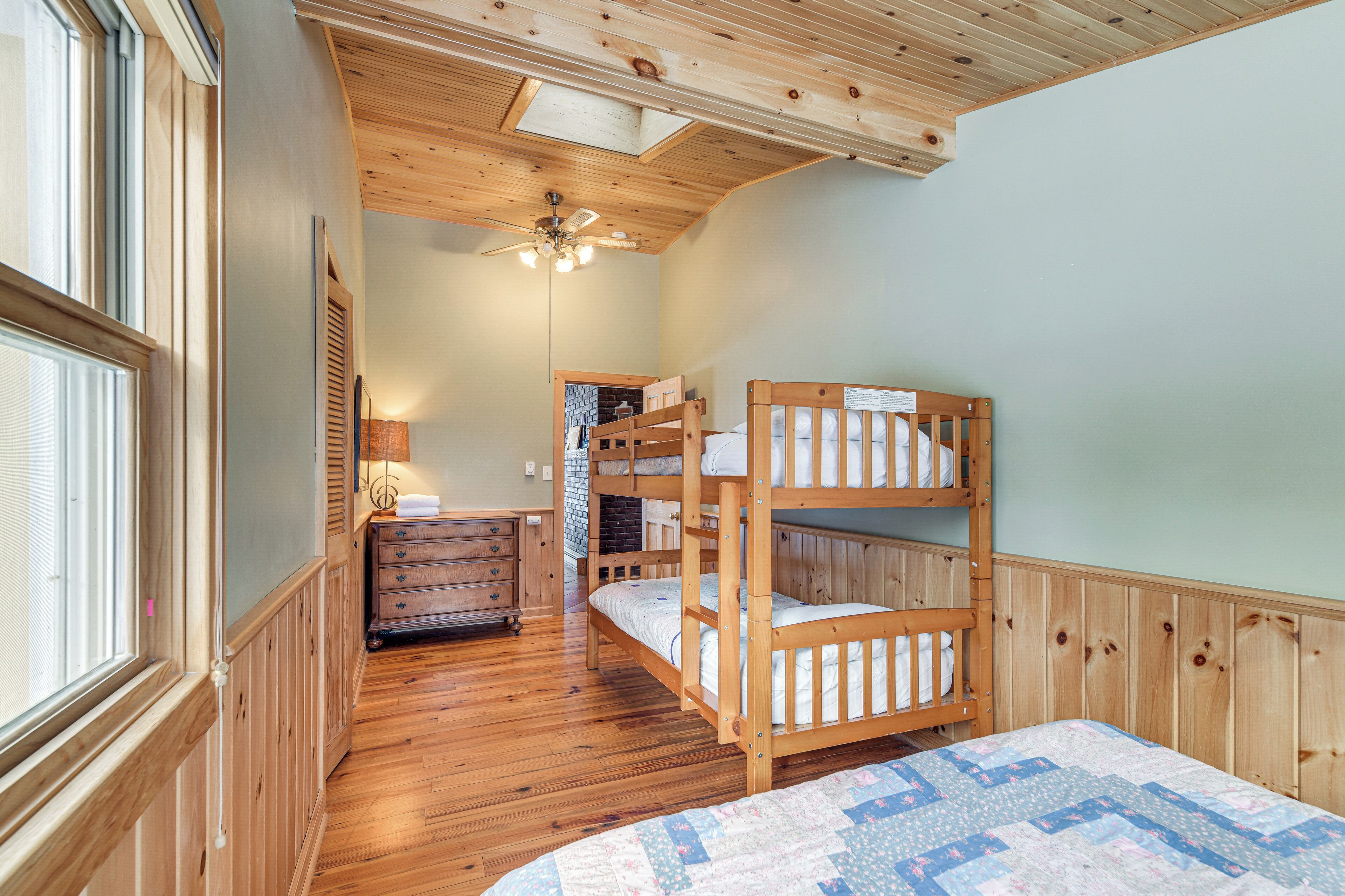 A room with wooden bunk beds, a dresser, a lamp, and a ceiling fan.