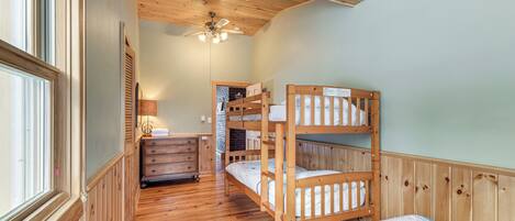 A room with wooden bunk beds, a dresser, a lamp, and a ceiling fan.