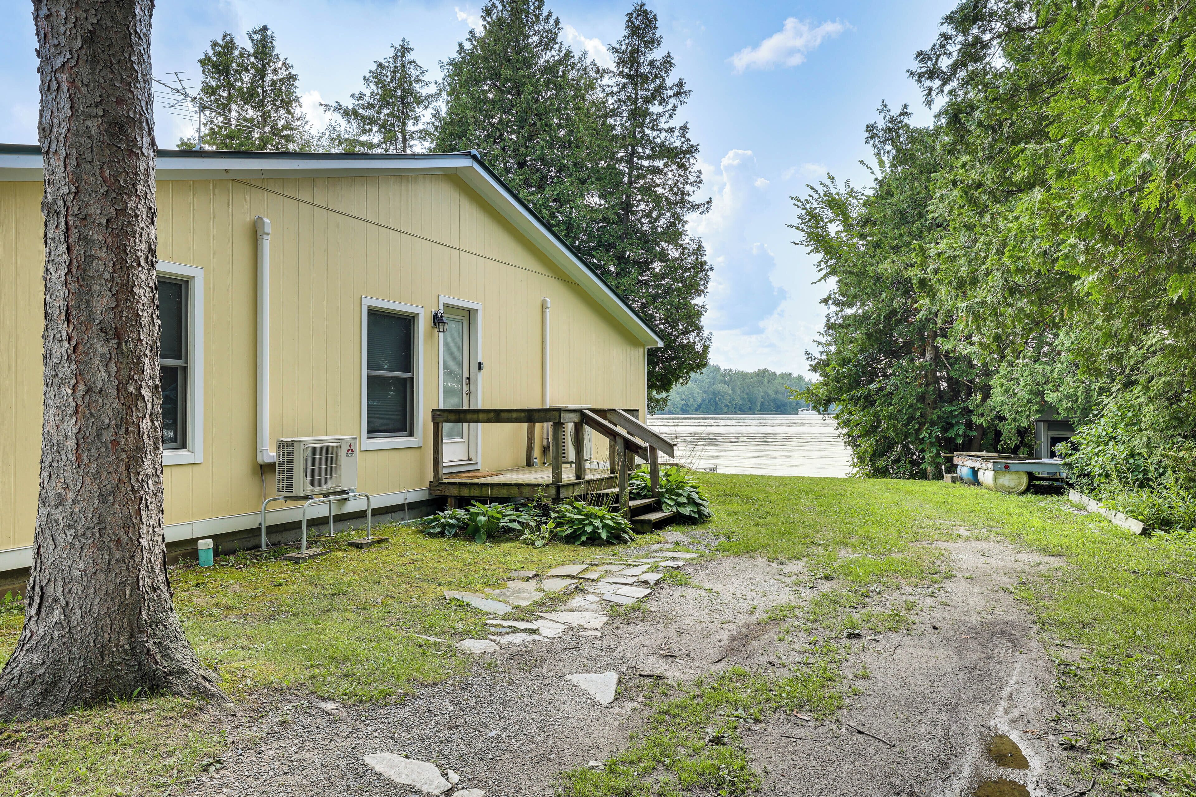 A yellow house with a porch, a stone pathway, and a view of a lake.
