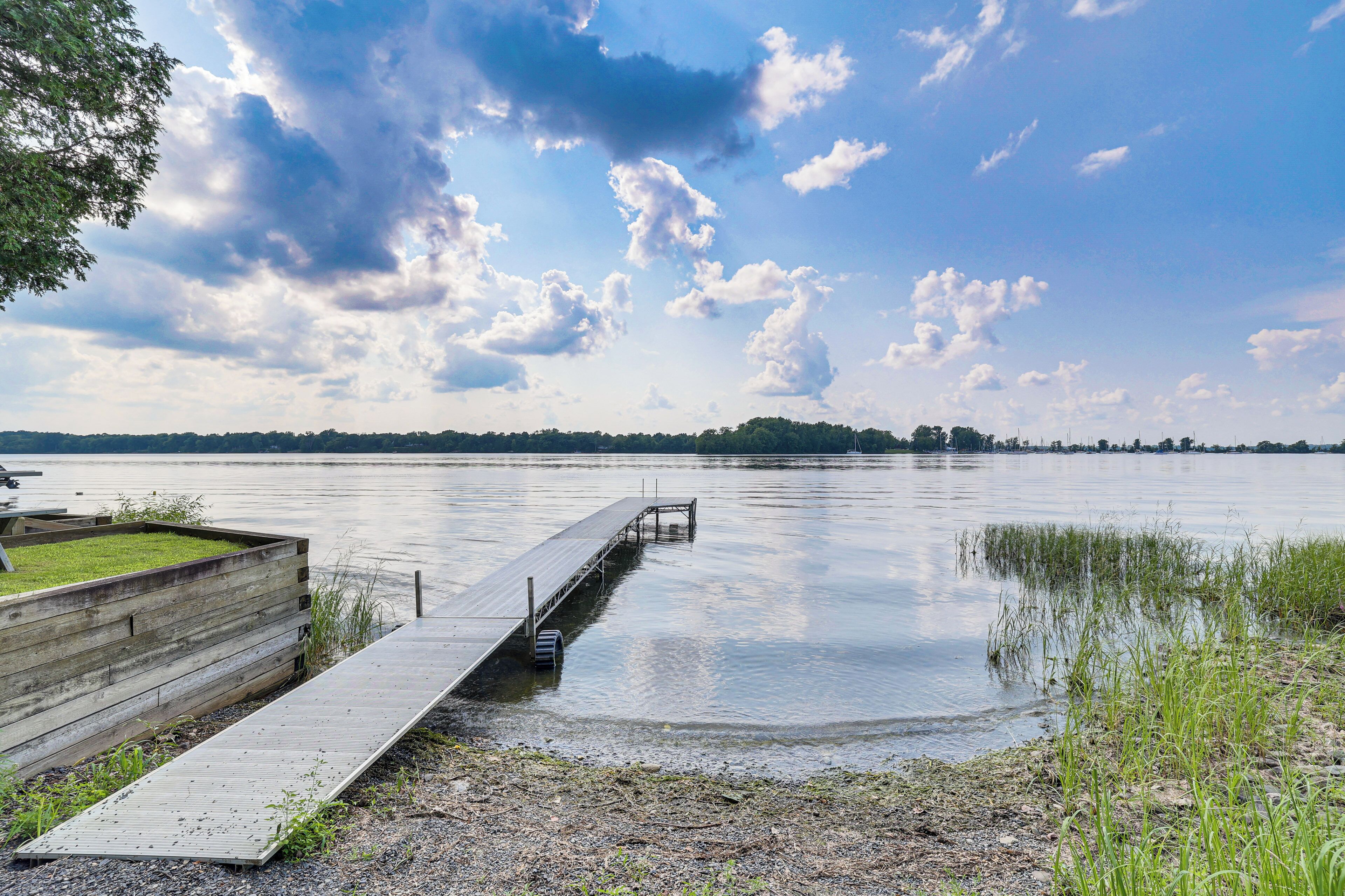 A wooden dock extending into calm water with a grassy area and trees in the background.