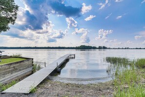 A wooden dock extending into calm water with a grassy area and trees in the background. - Waterfront North Hero Home w/ Screened Porch (North Hero)