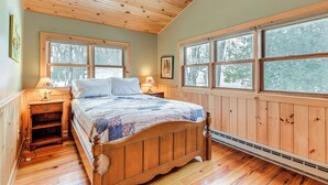 Een slaapkamer met houten lambrisering, een bed, twee nachtkastjes en grote ramen.
