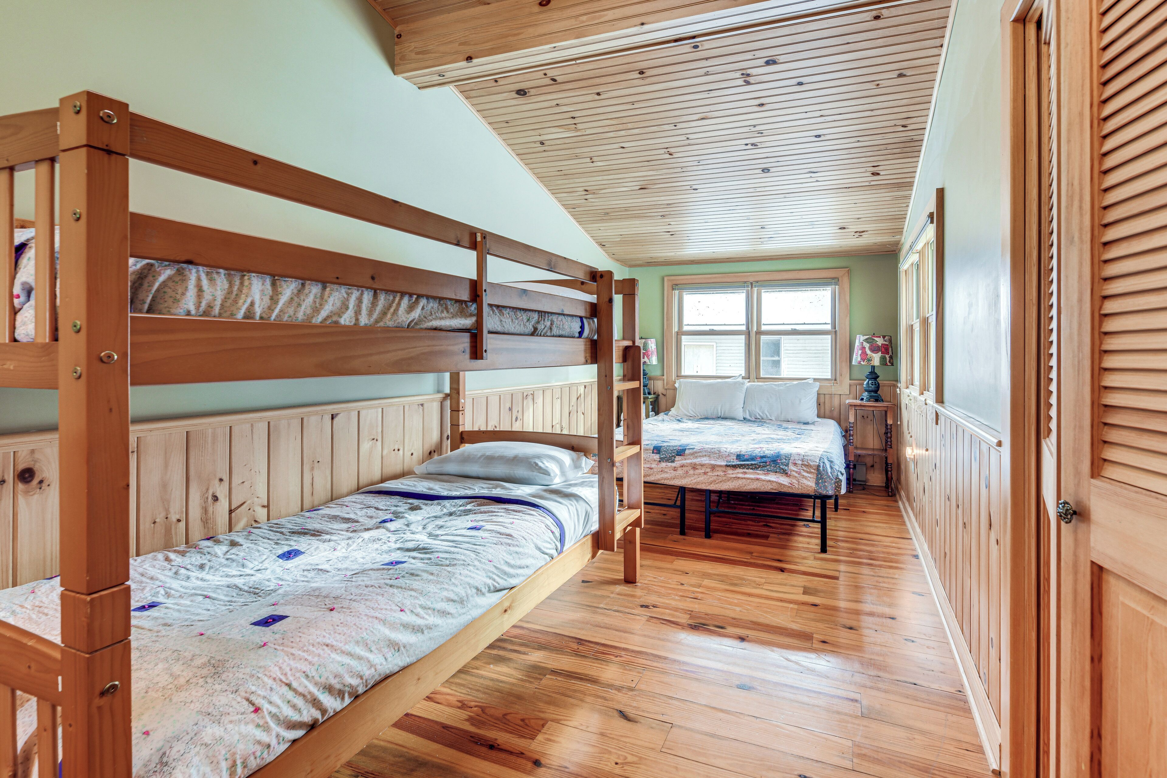 Ein Zimmer mit zwei Etagenbetten, Holzboden, einem Fenster mit Jalousien und einer Tür mit einem Holzpaneel.