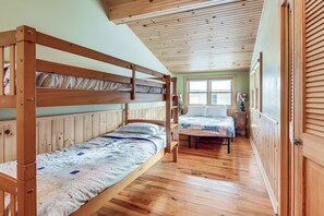 Une chambre avec deux lits superposés, un plancher en bois, une fenêtre avec des stores et une porte avec un panneau en bois.