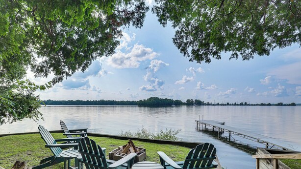 Een terras aan het meer met Adirondack-stoelen, een vuurkuil en een steiger die in het water uitsteekt.