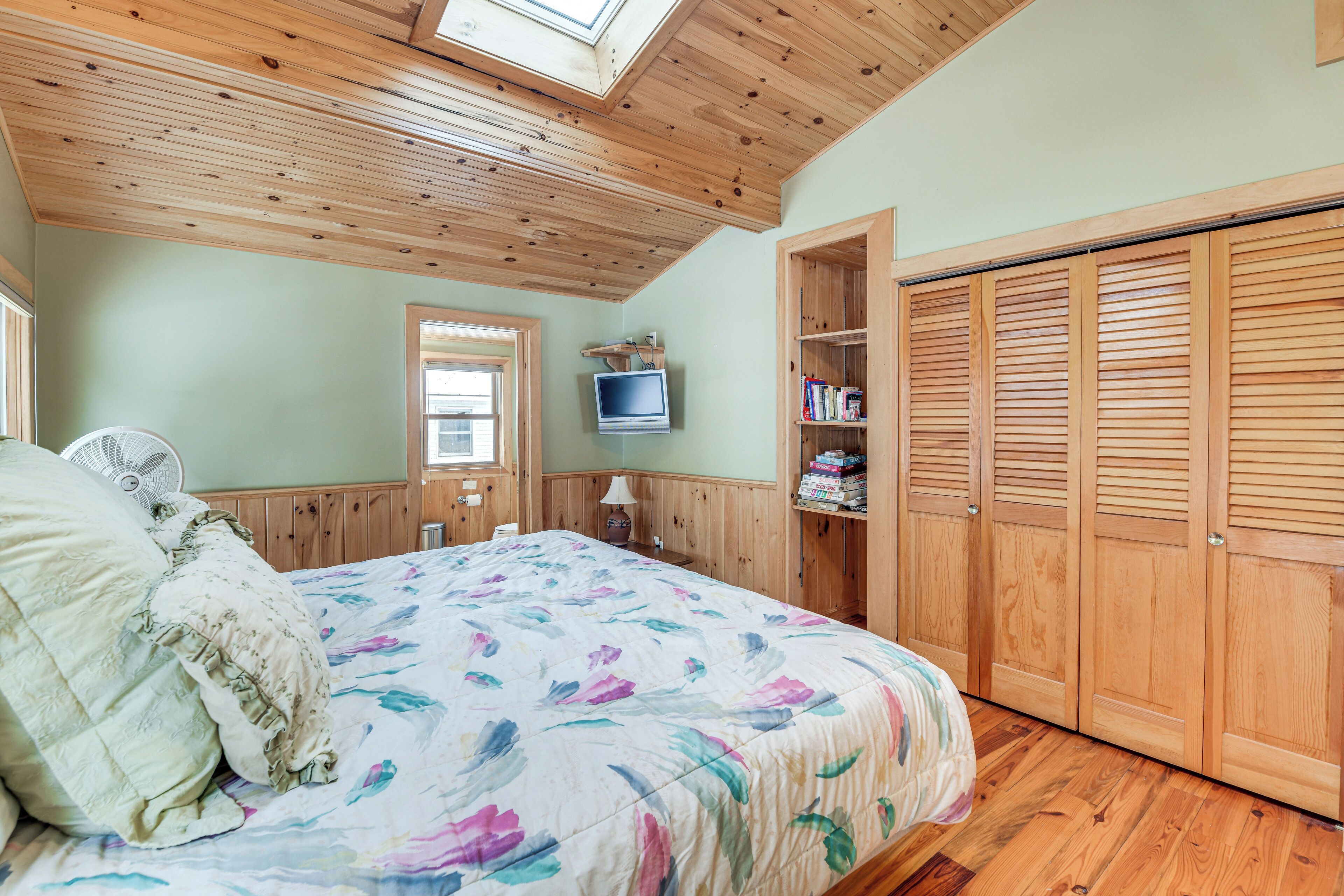 Ein Schlafzimmer mit Holzboden, einem Bett mit floraler Bettwäsche, einem Fernseher und Holzschränken.