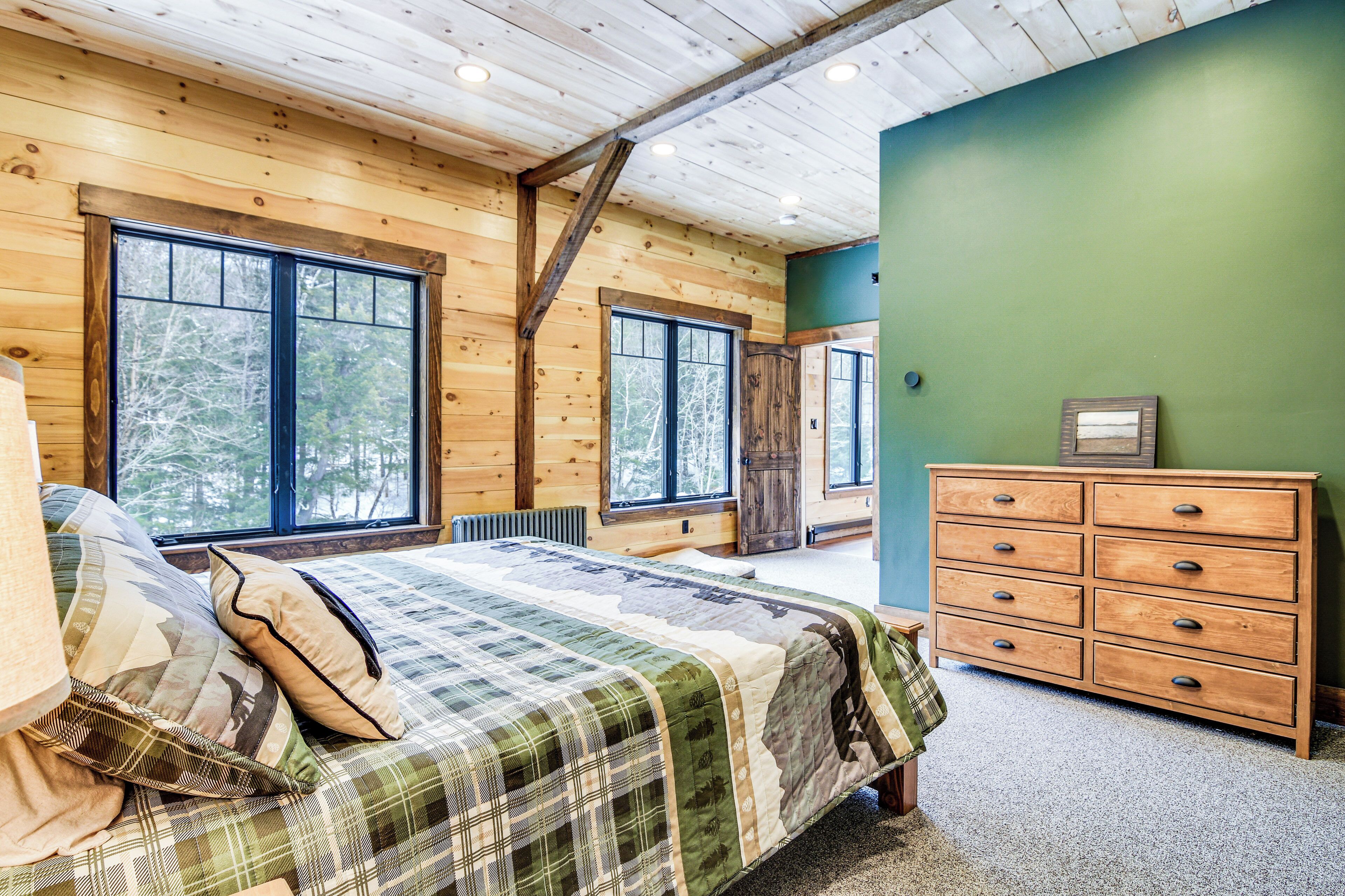 Un dormitorio de cabaña de madera con cama, cómoda y ventanas amplias.