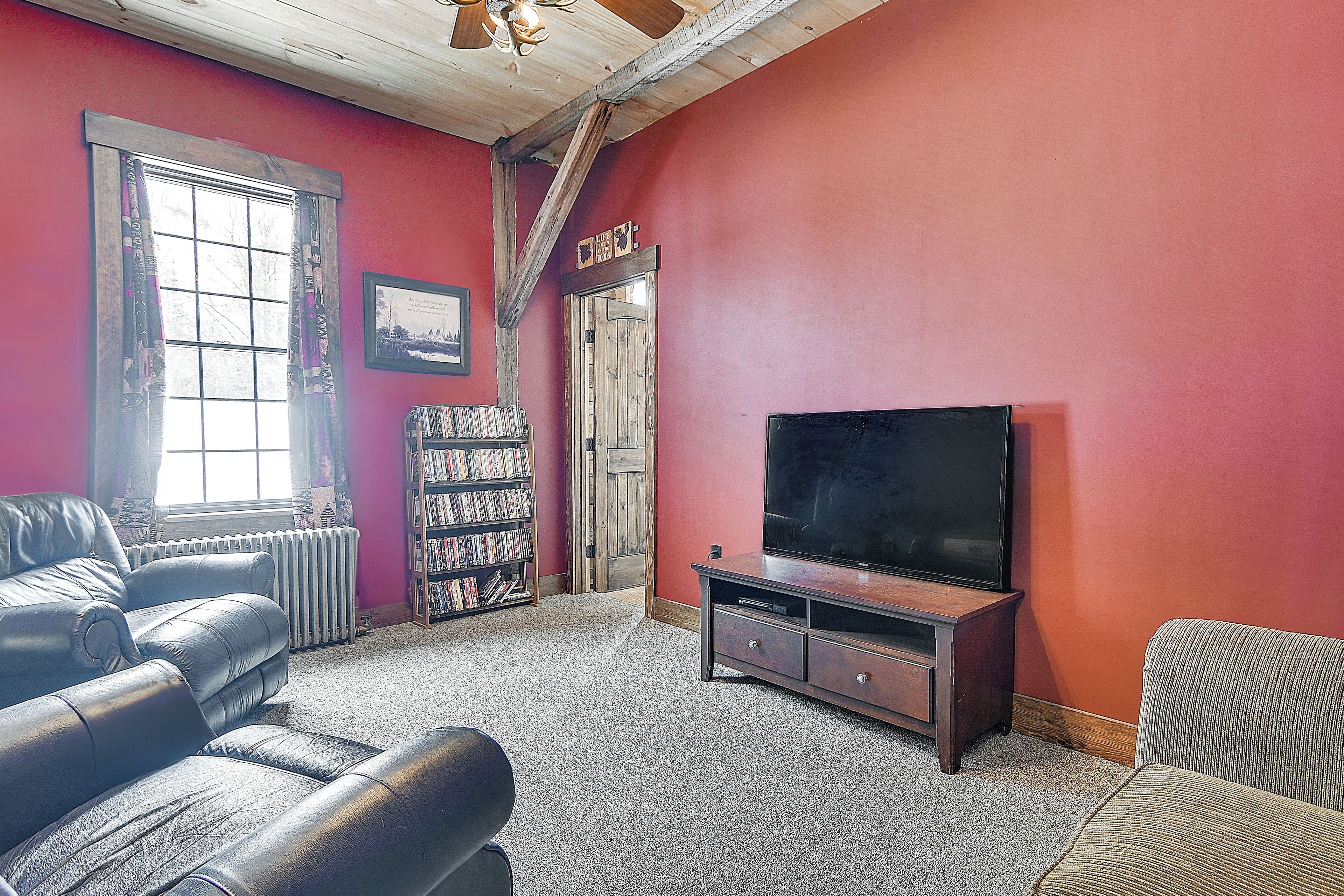 Un salon avec un mur rouge, un plafond en bois, un grand téléviseur à écran plat, une bibliothèque et une cheminée.