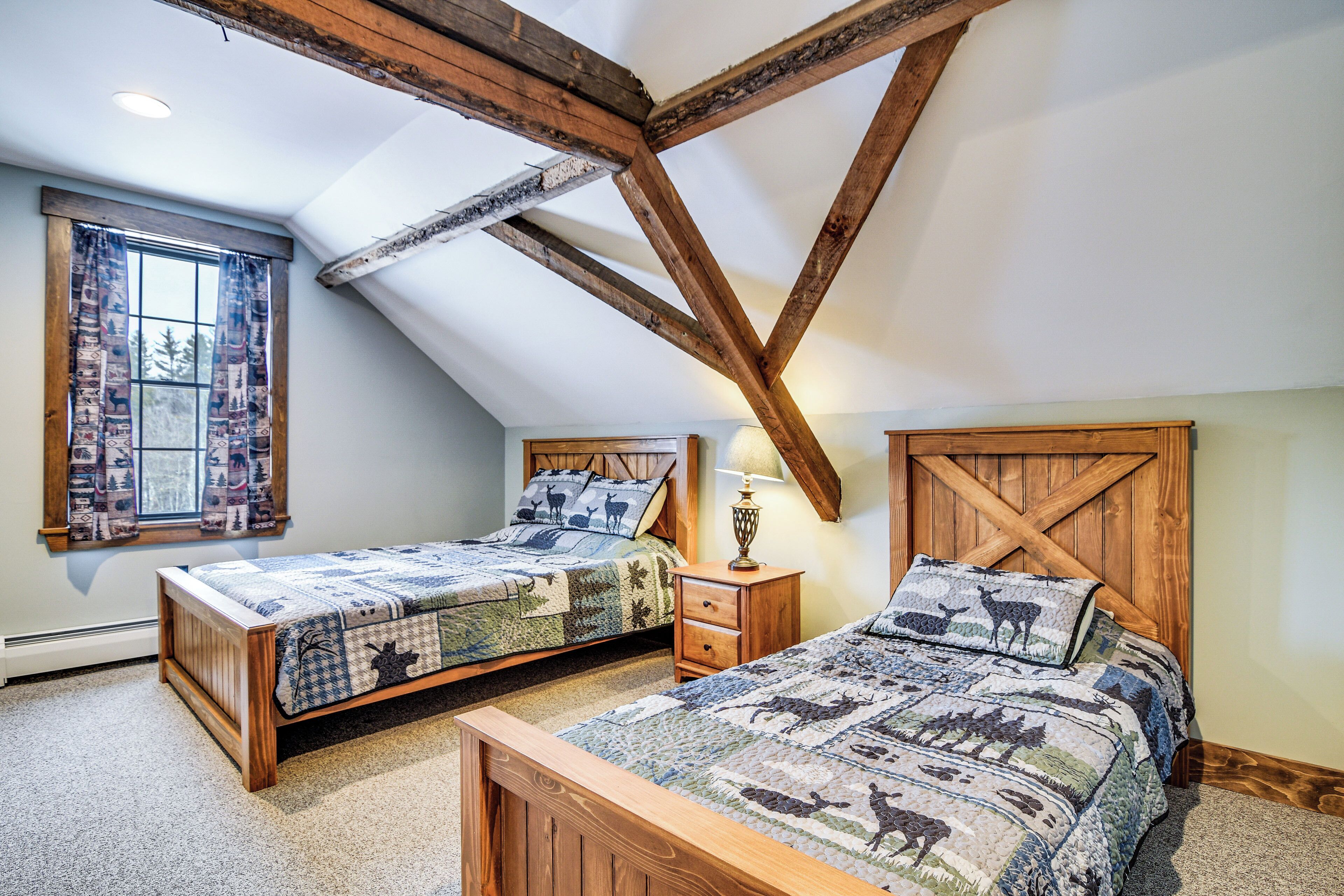 Une chambre avec deux lits en bois, une fenêtre ornée de rideaux à motifs et un plafond en pente avec des poutres apparentes.
