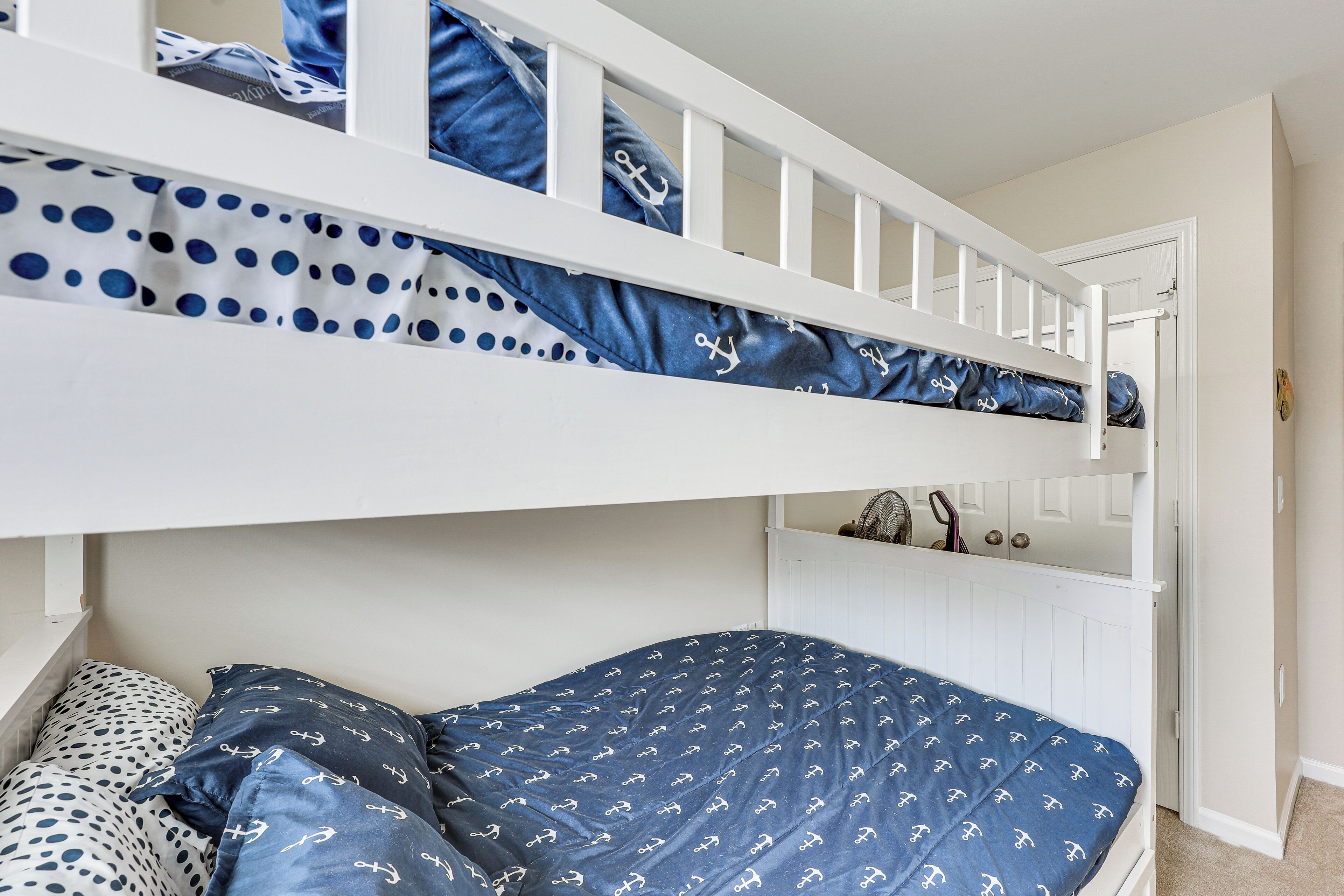 A bunk bed with a polka dot and anchor-patterned bedspread, white railings, and a white door.