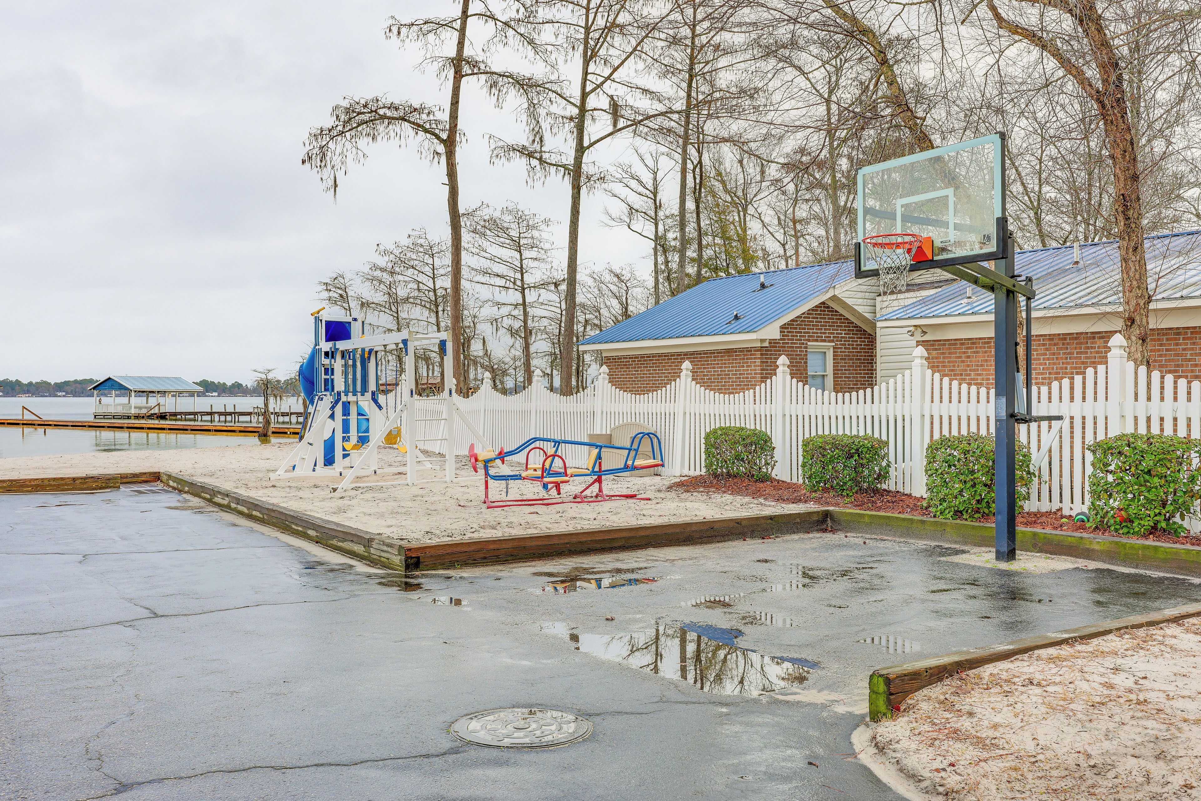 A playground with a basketball hoop, a seesaw, and a blue climbing structure.
