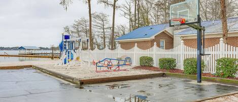 A playground with a basketball hoop, a seesaw, and a blue climbing structure.