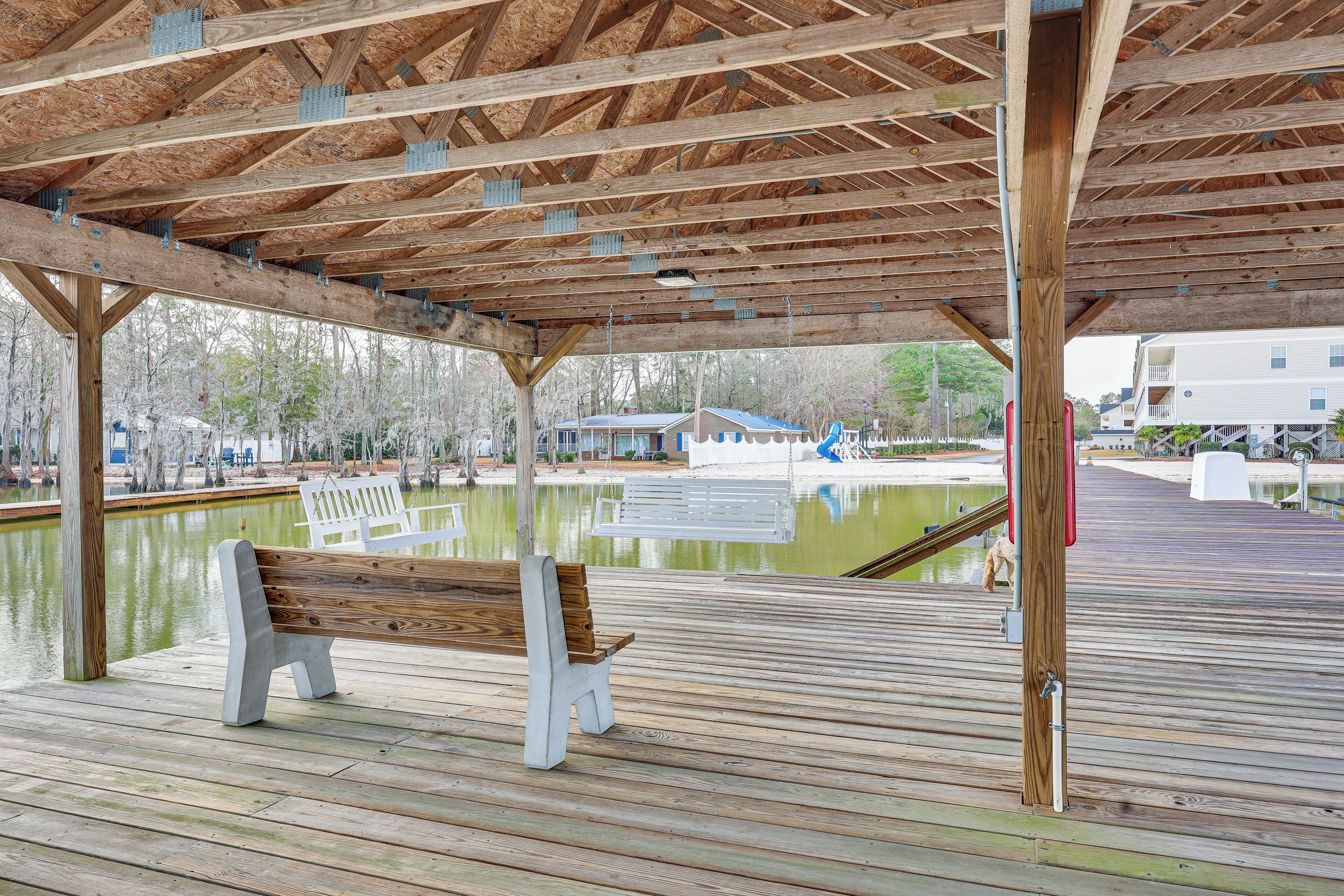 A wooden deck with a bench, a covered area, and a body of water in the background.