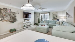 Una sala de estar con un sofá modular, un televisor de pantalla plana, un ventilador de techo y una decoración de red de pesca colgada en la pared.