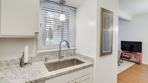 A modern kitchen with a granite countertop, stainless steel sink, and a window with blinds. - Walk to Lake Michigan - South Haven Condo! (South Haven)
