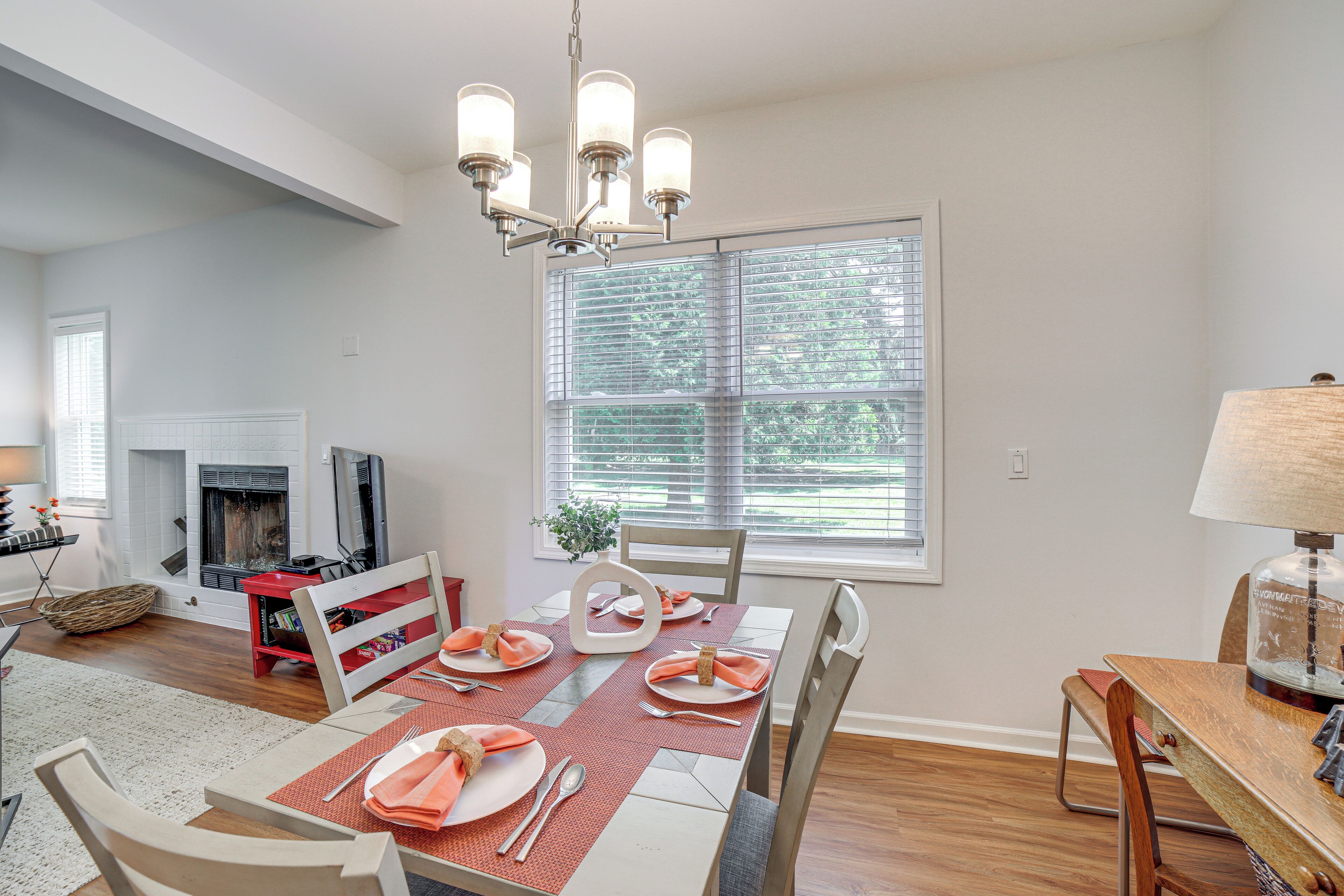 A dining area with a table set for four, a chandelier, and a fireplace in the background.