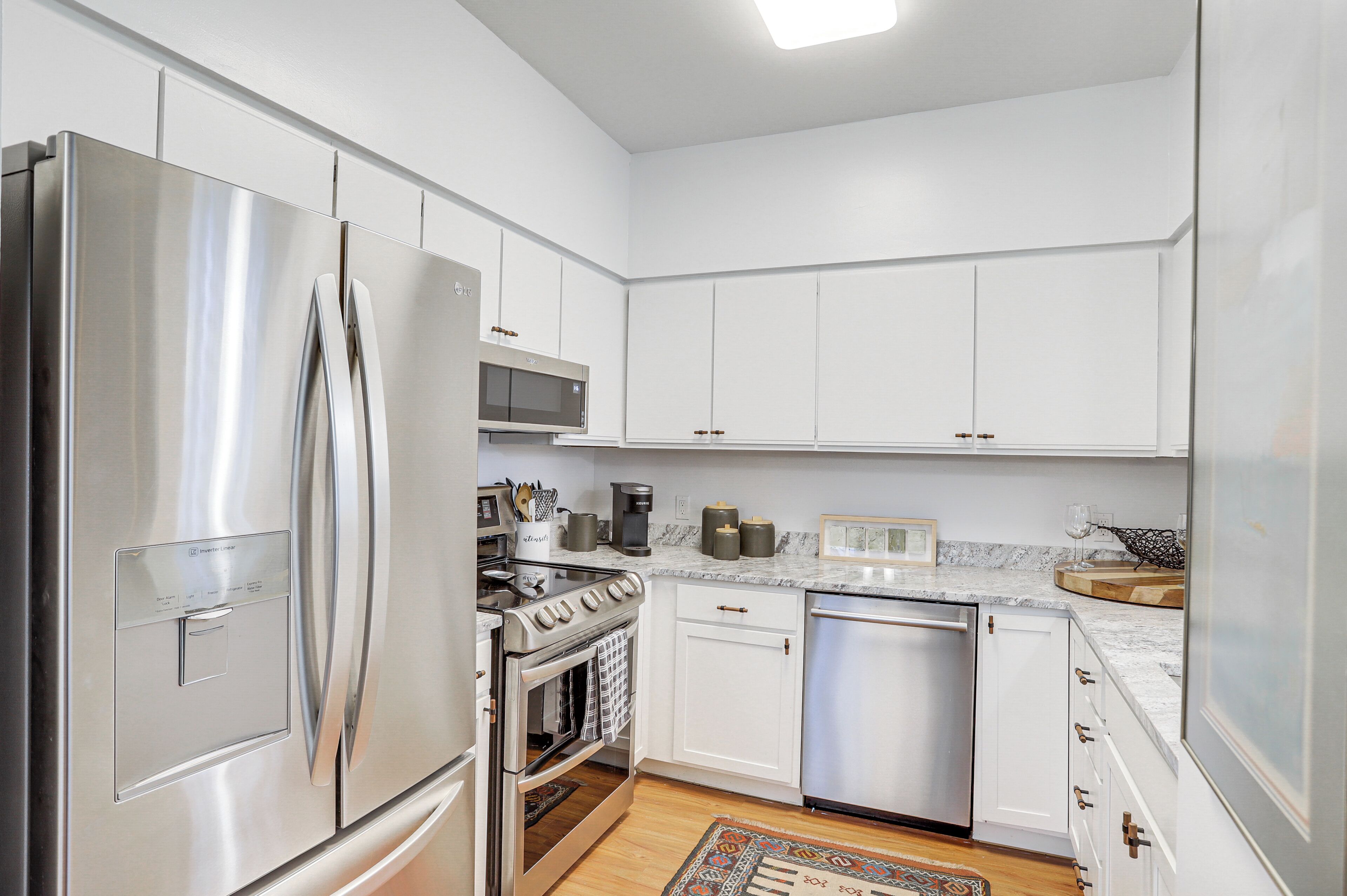 A modern kitchen with stainless steel appliances, white cabinetry, and a marble countertop.