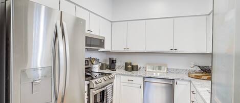 A modern kitchen with stainless steel appliances, white cabinetry, and a marble countertop.
