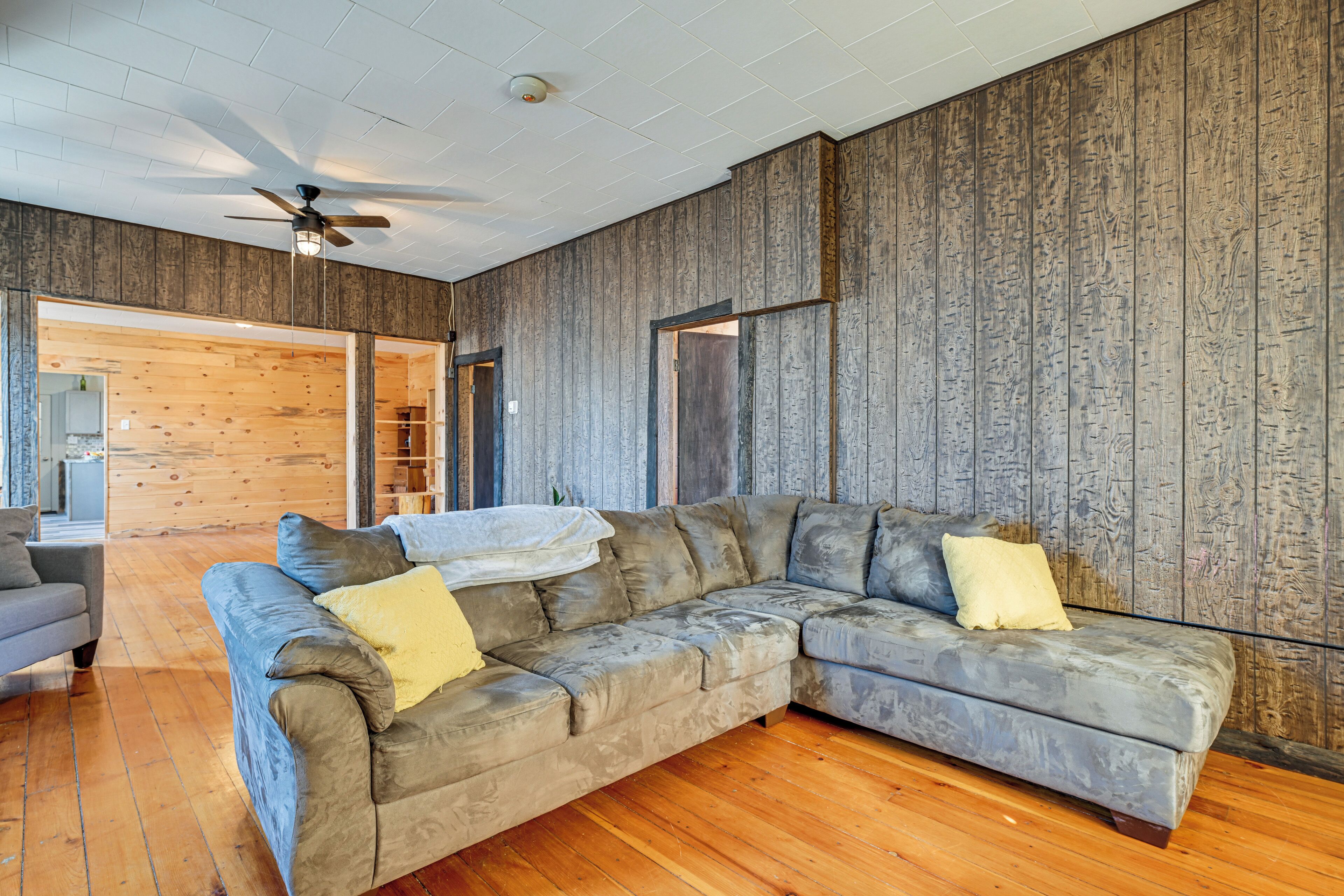 A modern living room with a sectional sofa, wooden walls, and a ceiling fan.