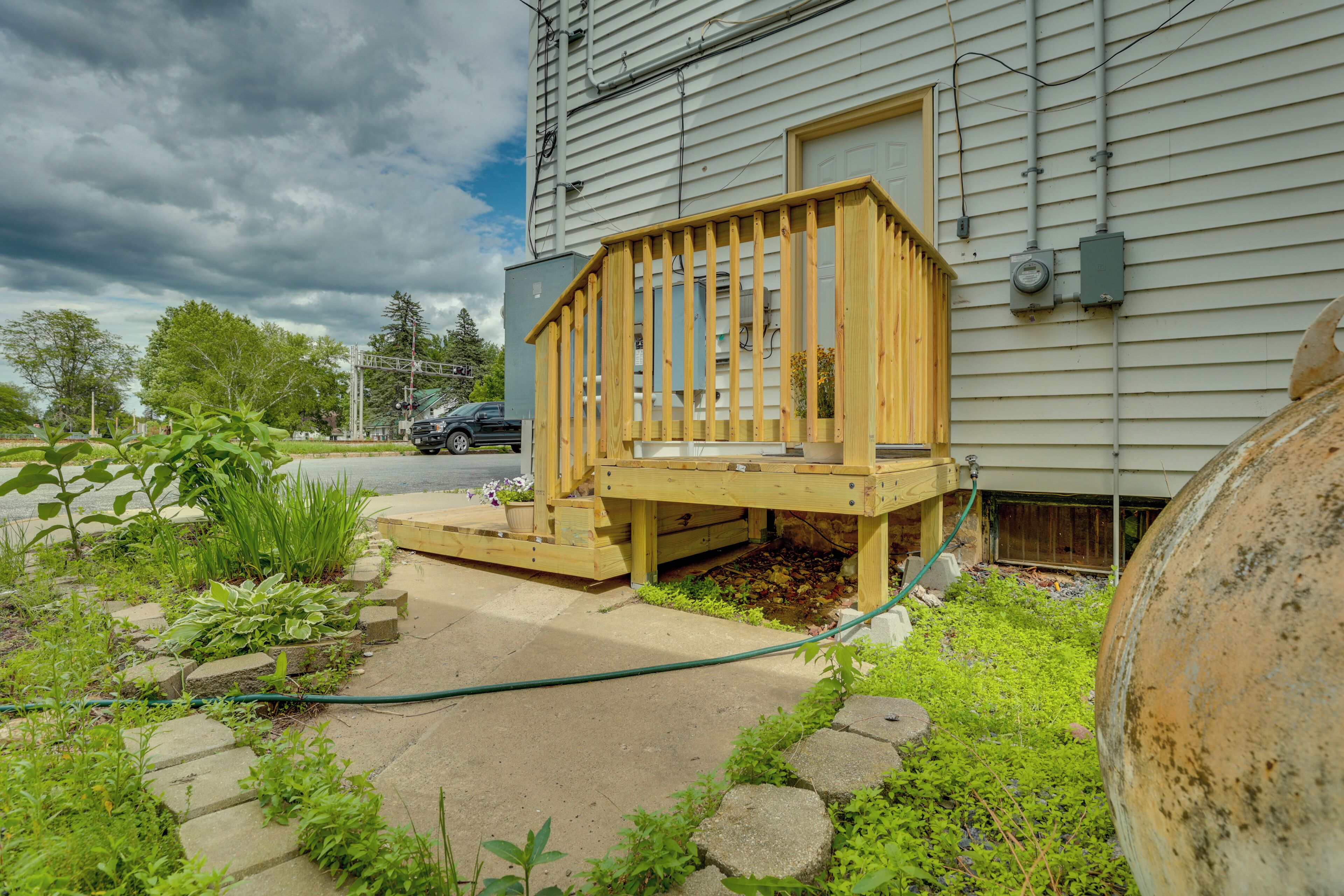 A wooden deck with a small porch, a concrete pathway, and a garden area with plants and a large pot.