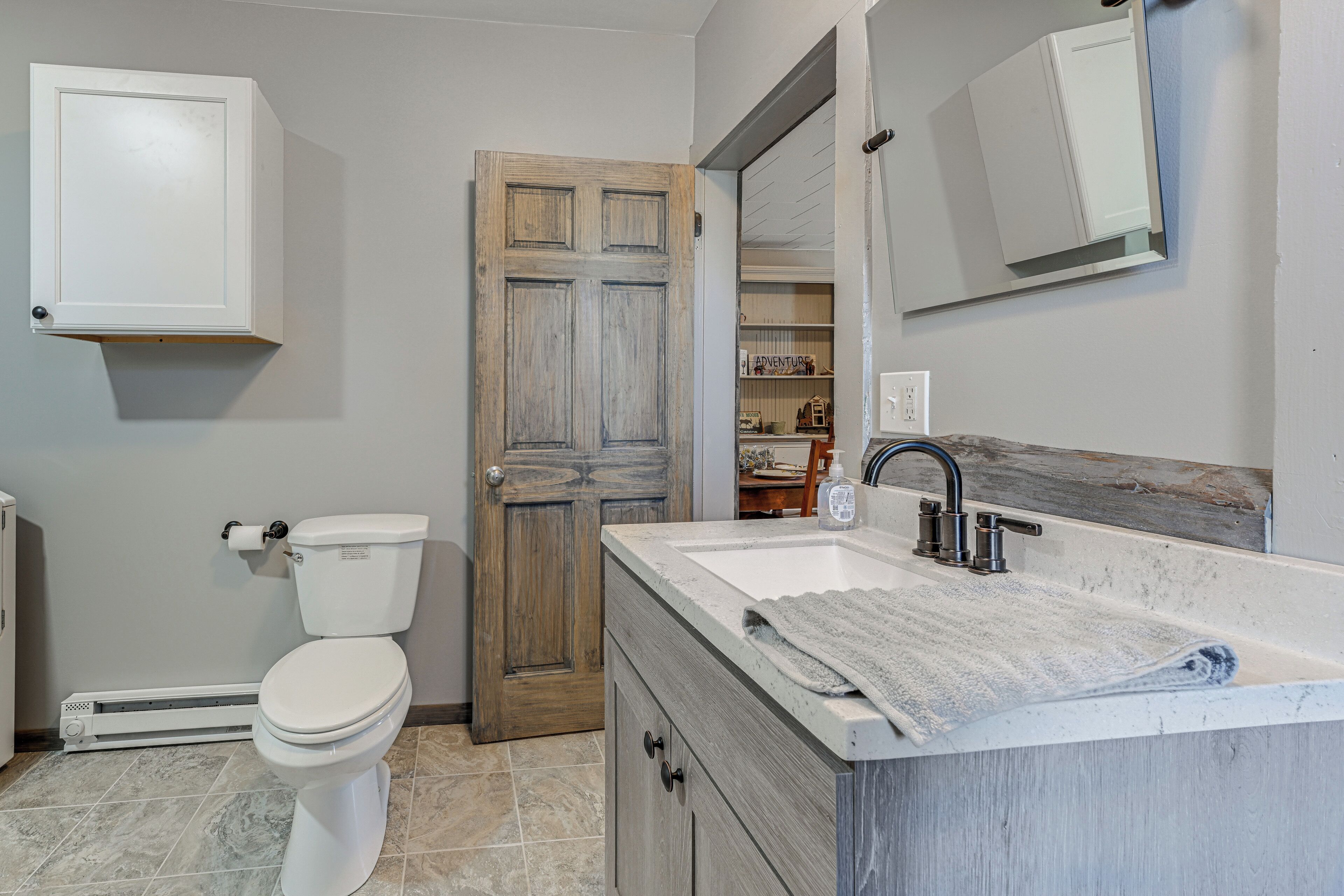A bathroom with a toilet, a wooden door, a white cabinet, a sink with a towel, and a mirror.