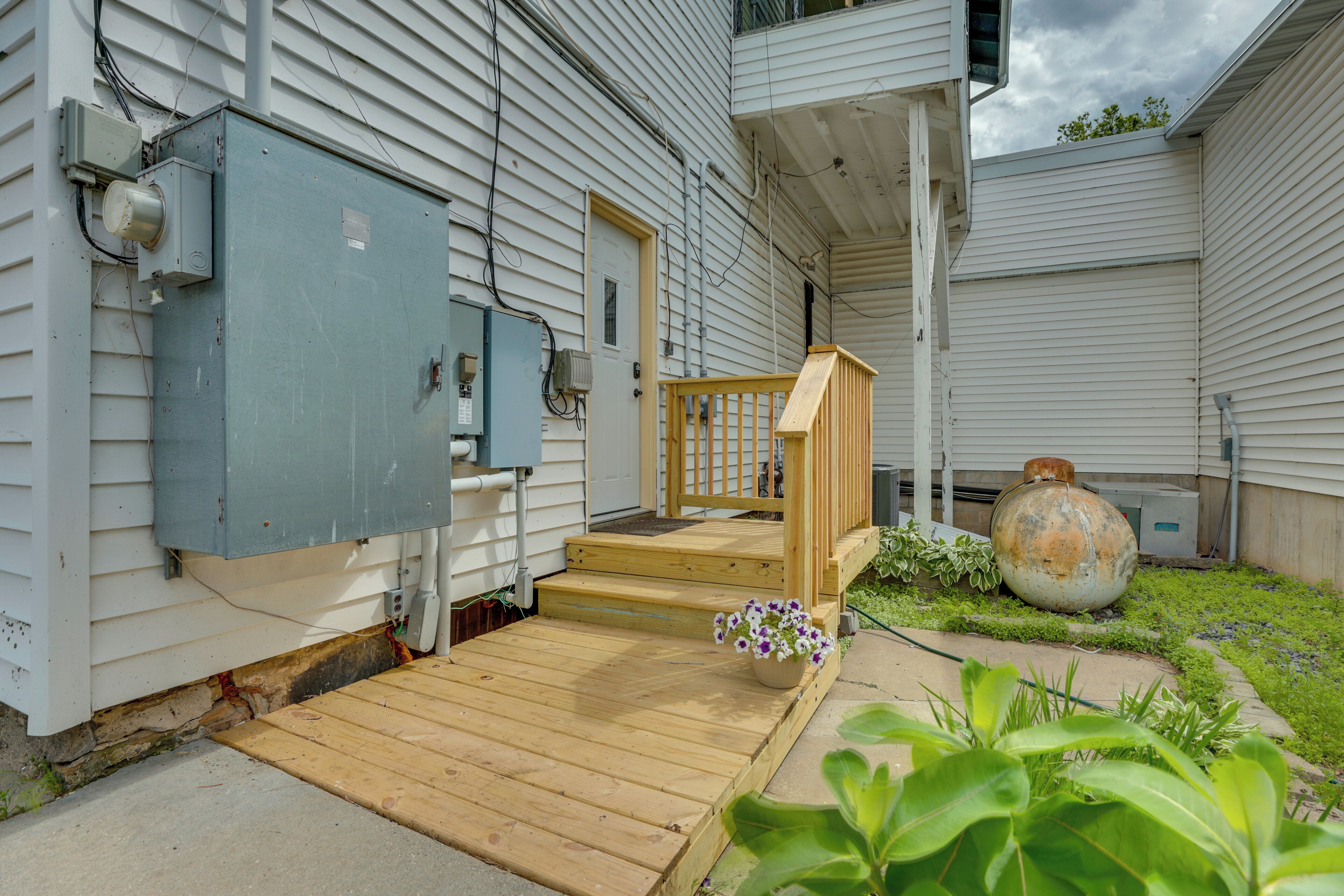 A house with a wooden front porch, a large electrical box, and a large decorative pot.