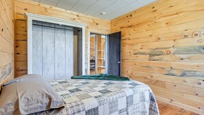 A bedroom with wooden walls, a bed with a quilt, a green throw blanket, and a door leading to another room. - Lyndon Station Retreat ~ 9 Mi to Wisconsin Dells! (Lyndon Station)