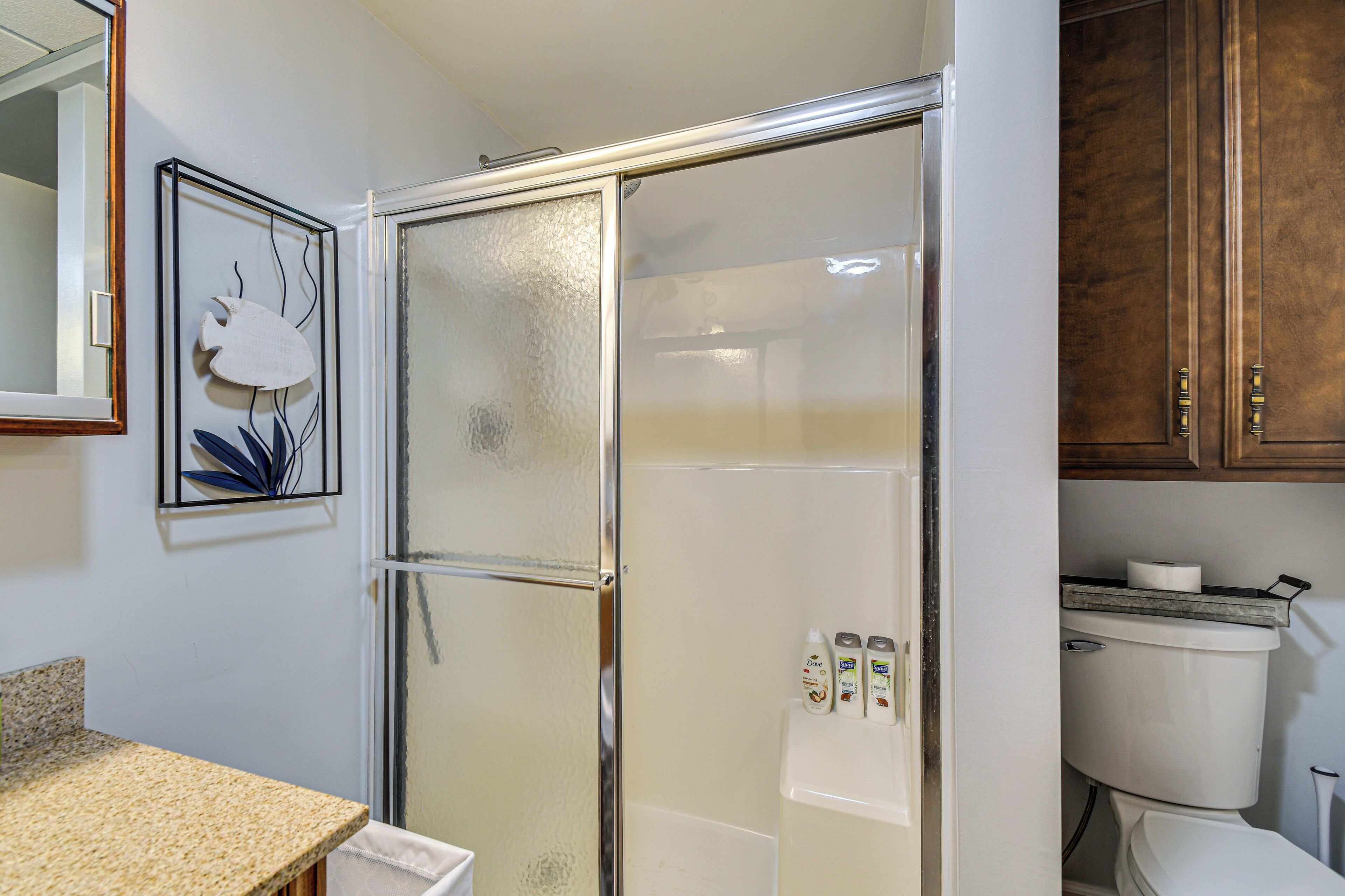 Un baño con cabina de ducha de vidrio, inodoro y lavamanos con encimera de granito.